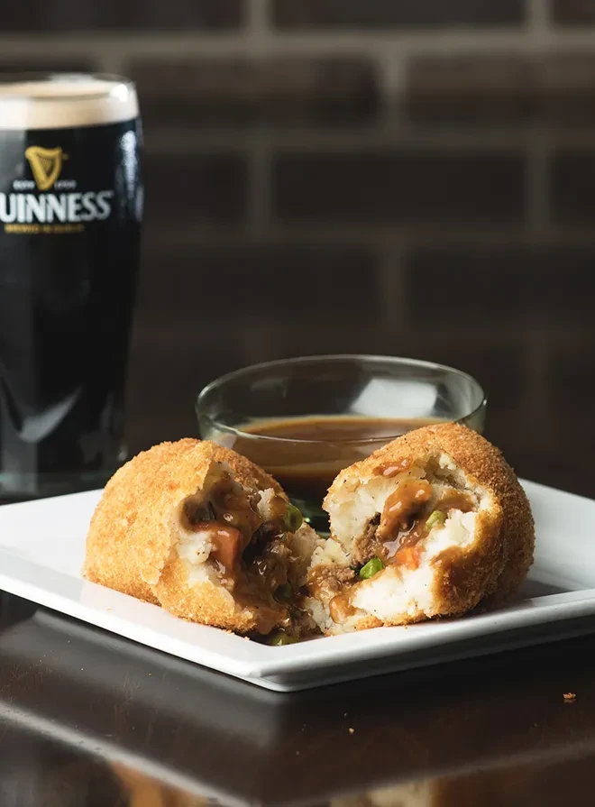 Deep-fried balls with meat, vegetables, and gravy, alongside Guinness.