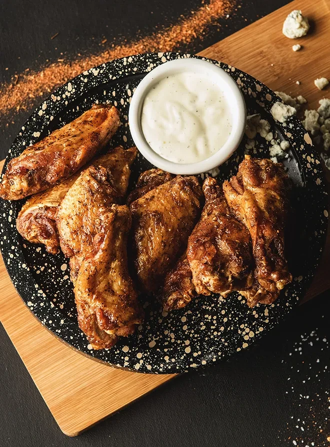 Golden-brown seasoned chicken wings, creamy dip, and scattered blue cheese.