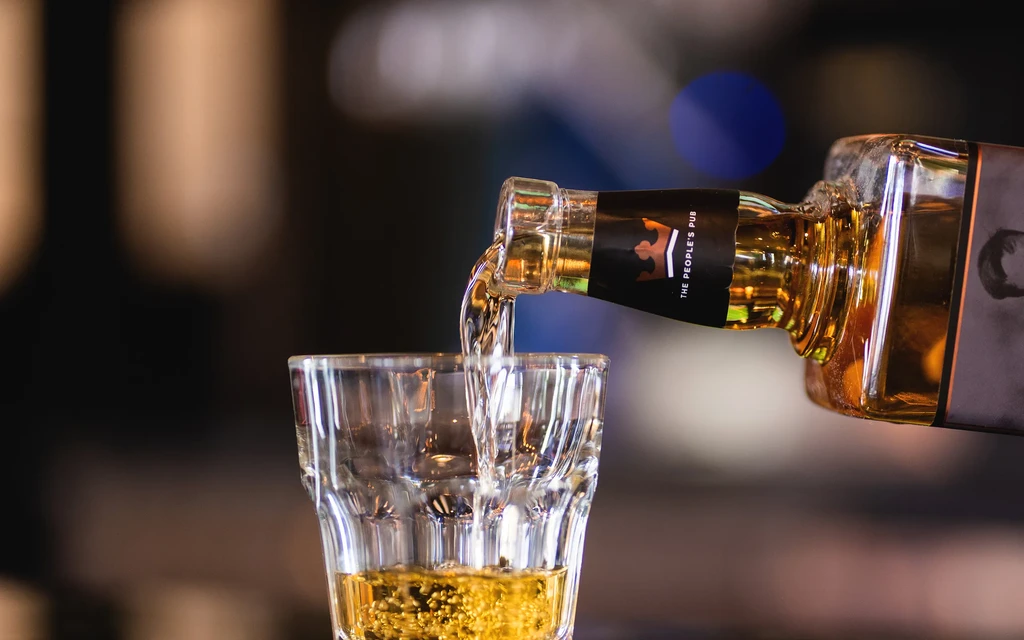 Amber spirit pours from a crown-labeled bottle into a glass.
