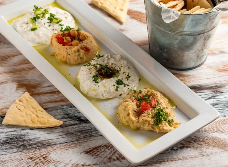 Four distinct dips with pita bread on a rustic wooden table.