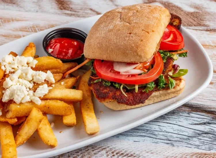 Hearty fried sandwich, cheesy wedge fries, and ketchup on a wooden table.