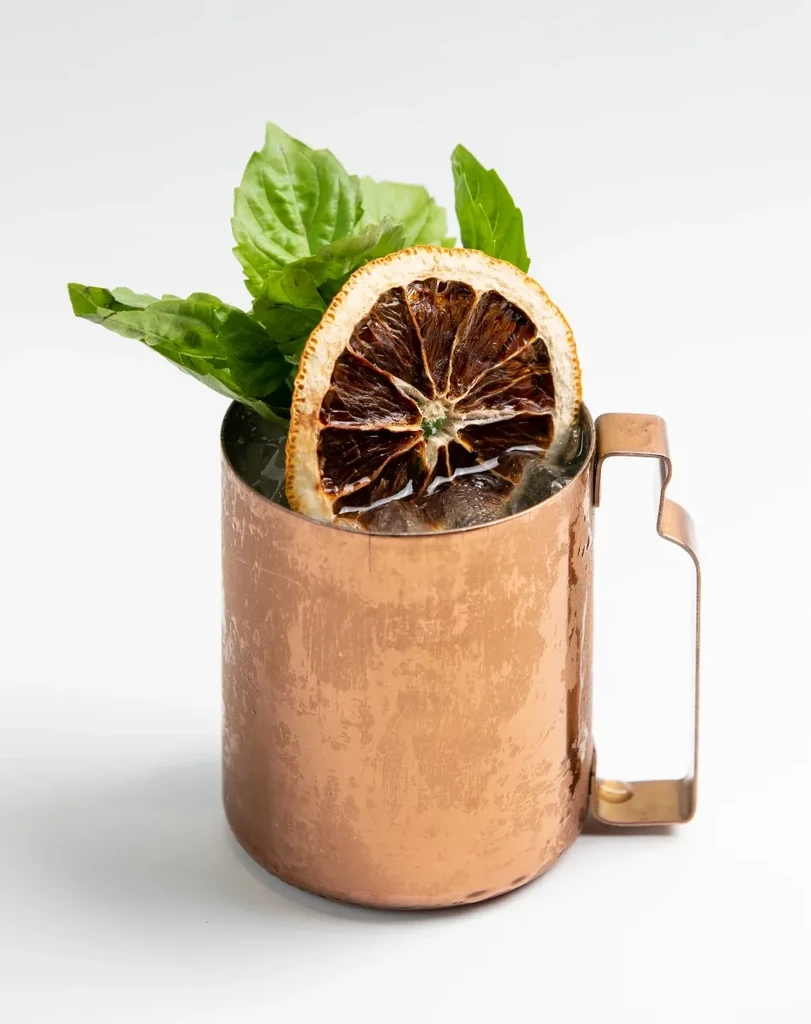 Hammered copper mug cocktail with dried orange and basil.