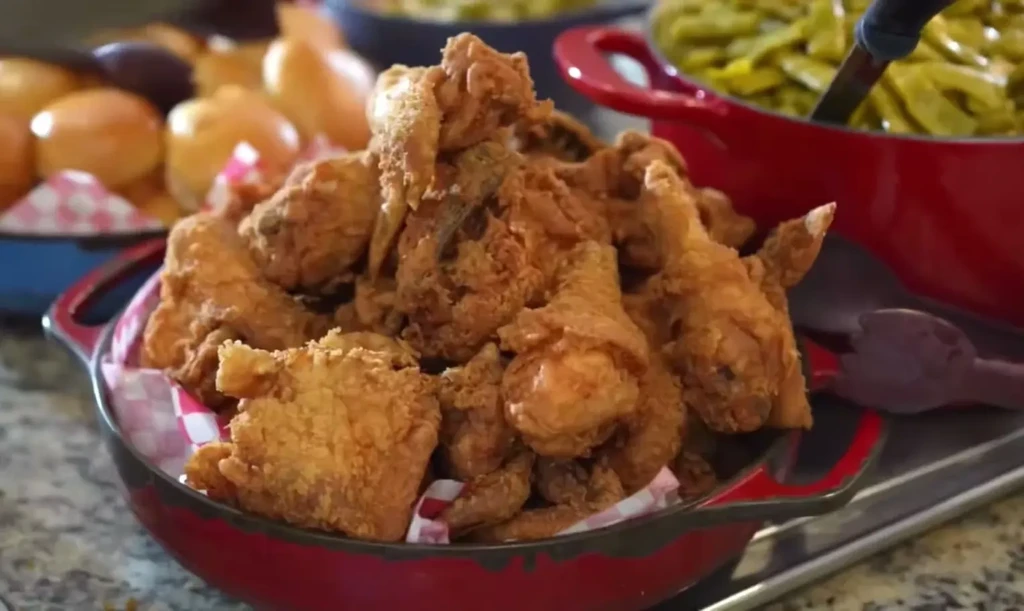 Red cast-iron bowl overflowing with crispy fried chicken and side dishes.