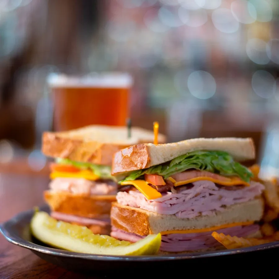 Club sandwich halves, pickle spear, and waffle fries on dark plate.