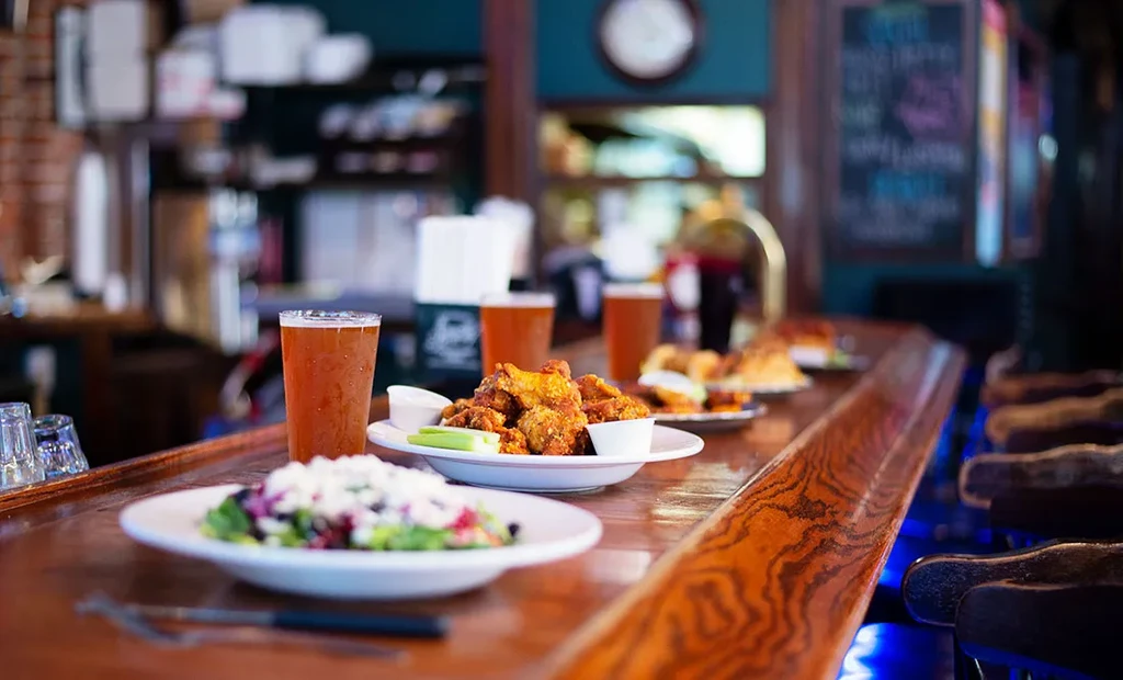Beer, salad, and chicken wings on a polished wooden bar counter.