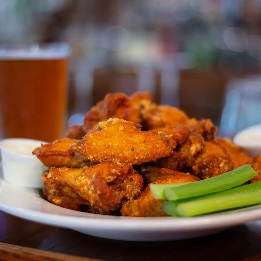Piled crispy golden chicken wings, celery, dipping sauce, and beer.