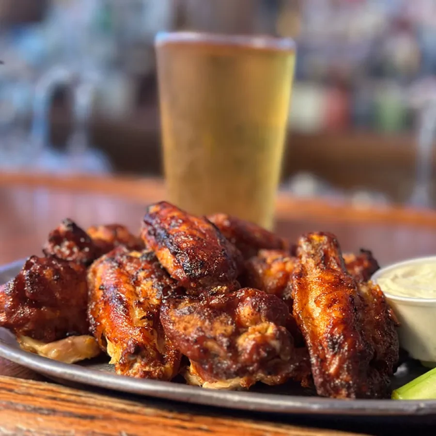 Plate of dark glazed chicken wings with dressing, celery, and beer.