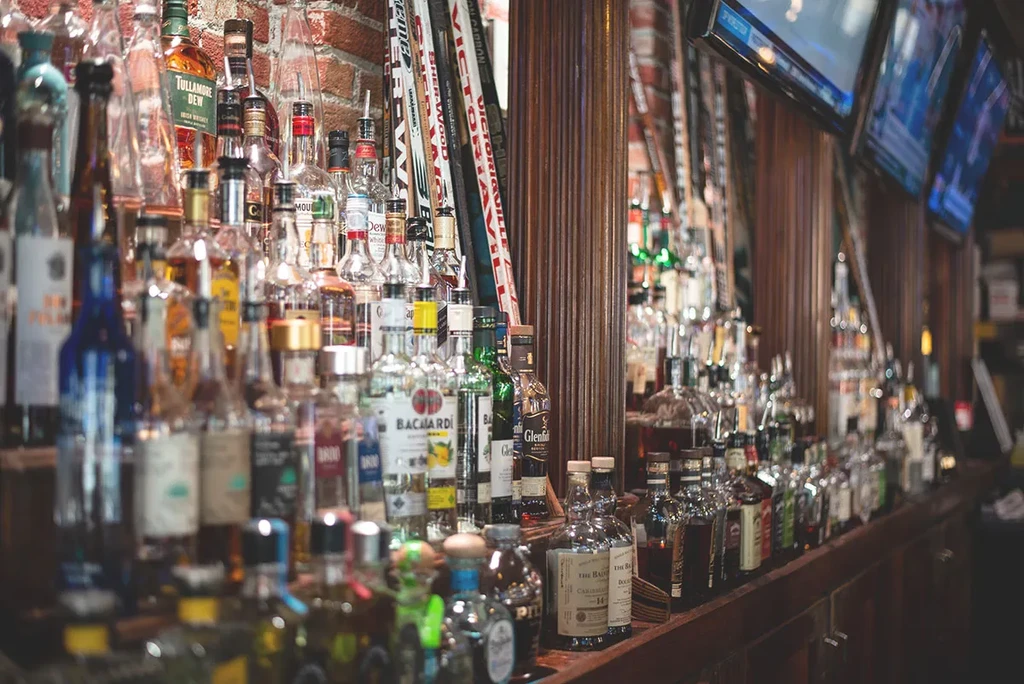 Well-stocked sports bar with spirit bottles, hockey sticks, and TVs.