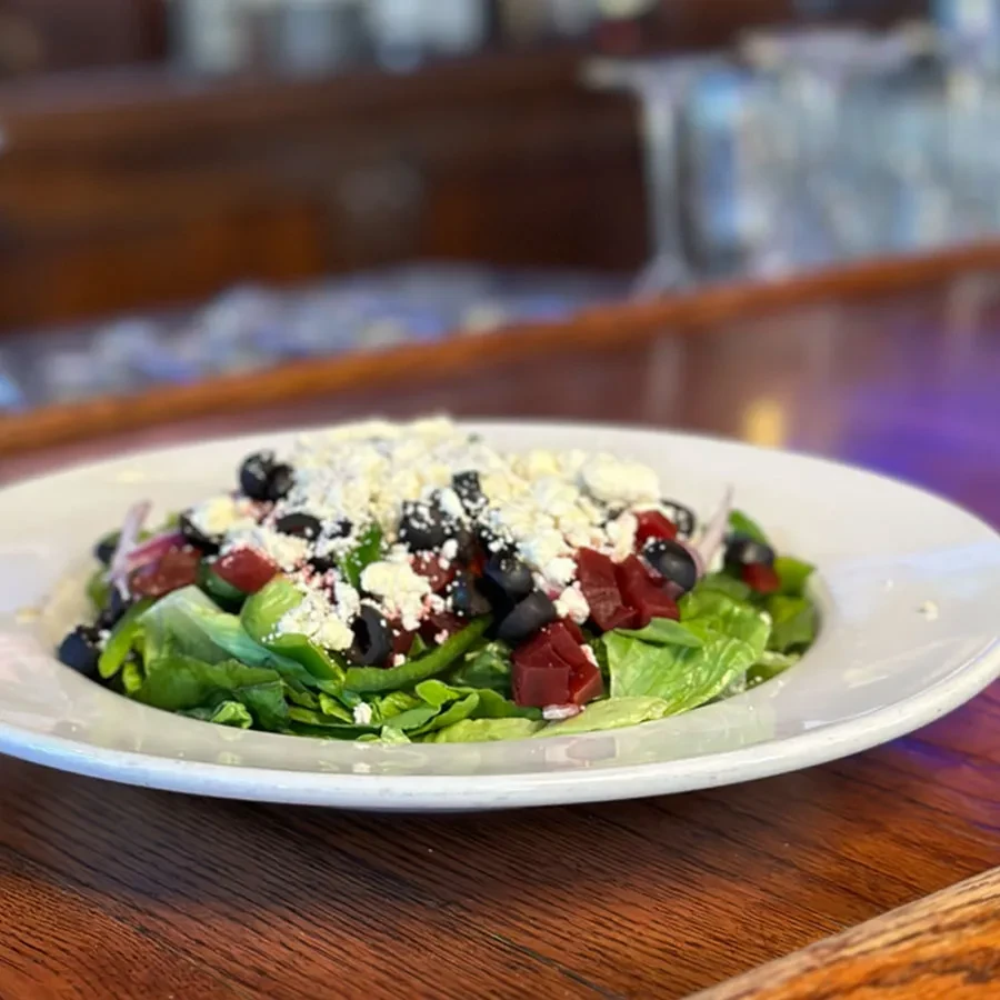 Fresh salad with lettuce, feta, olives, and red ingredients on wood.