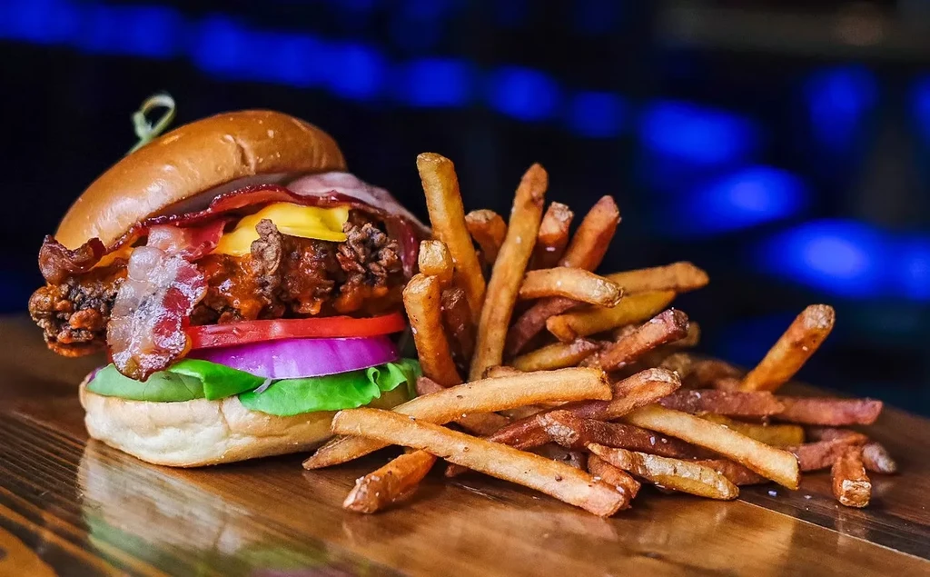 Gourmet burger, golden french fries, rustic wood, blue bokeh background.