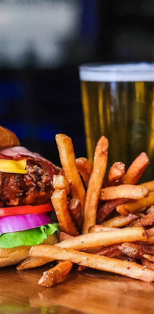 Loaded burger with fries and a drink on a wooden surface.