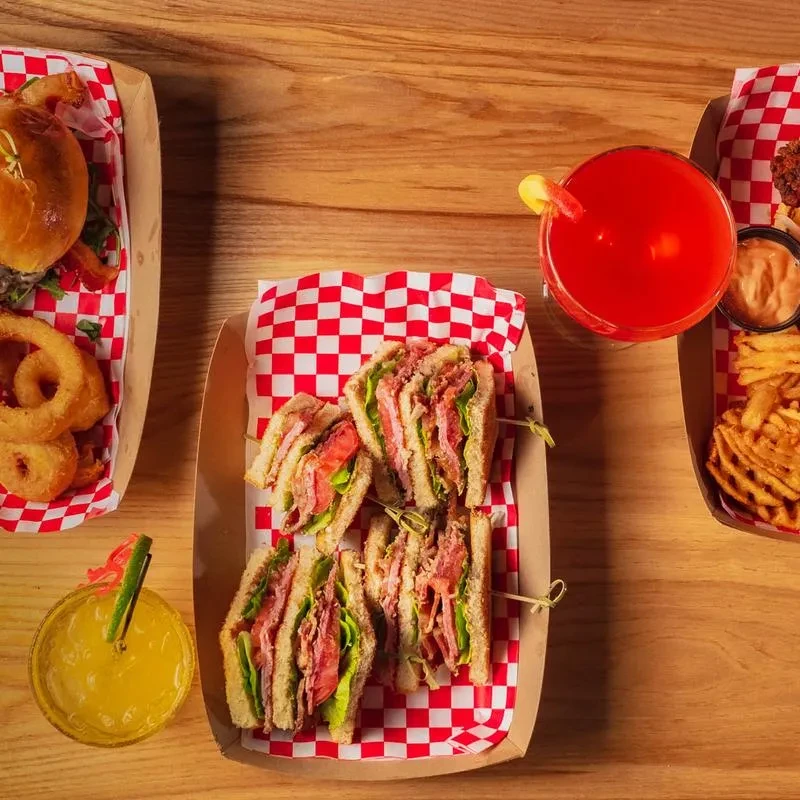 Flat lay of club sandwich, burger, fries, onion rings, and cocktails.
