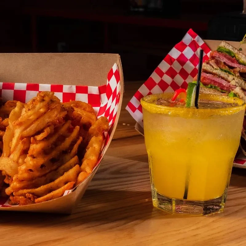 Close-up of golden waffle fries and yellow cocktail on wooden table.