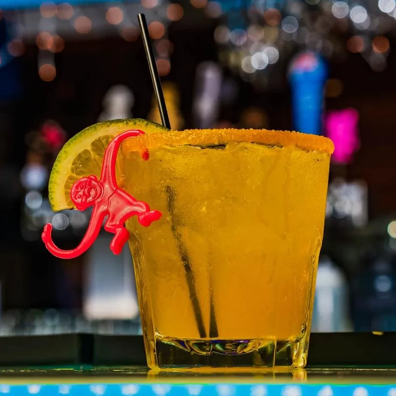 Yellow-orange cocktail in a rimmed rocks glass with lime and monkey stirrer.