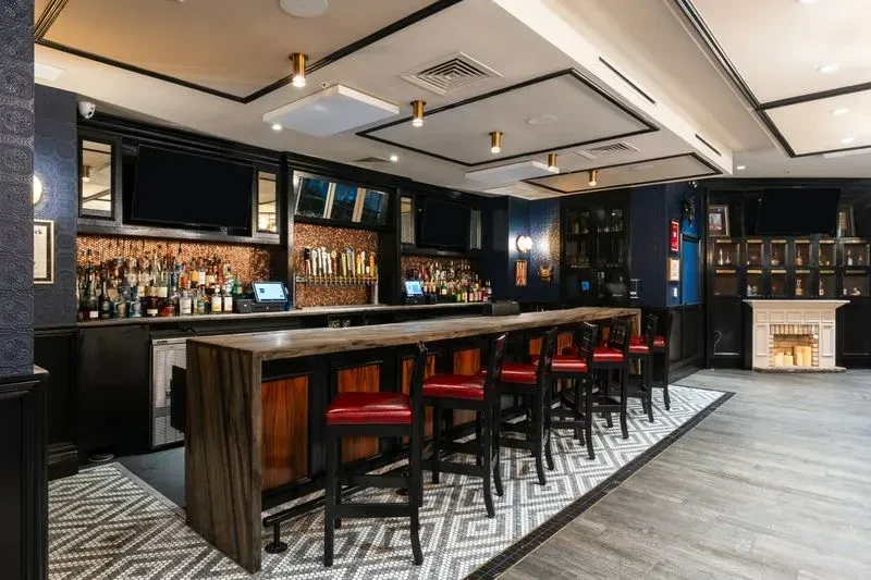 Well-appointed restaurant bar with wood counter, taps, red stools, and fireplace.