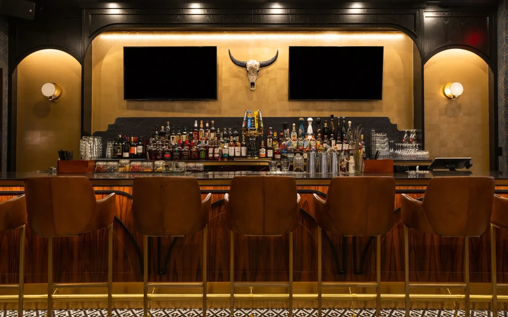 Empty upscale bar with stocked back bar, bull skull, and two TVs.