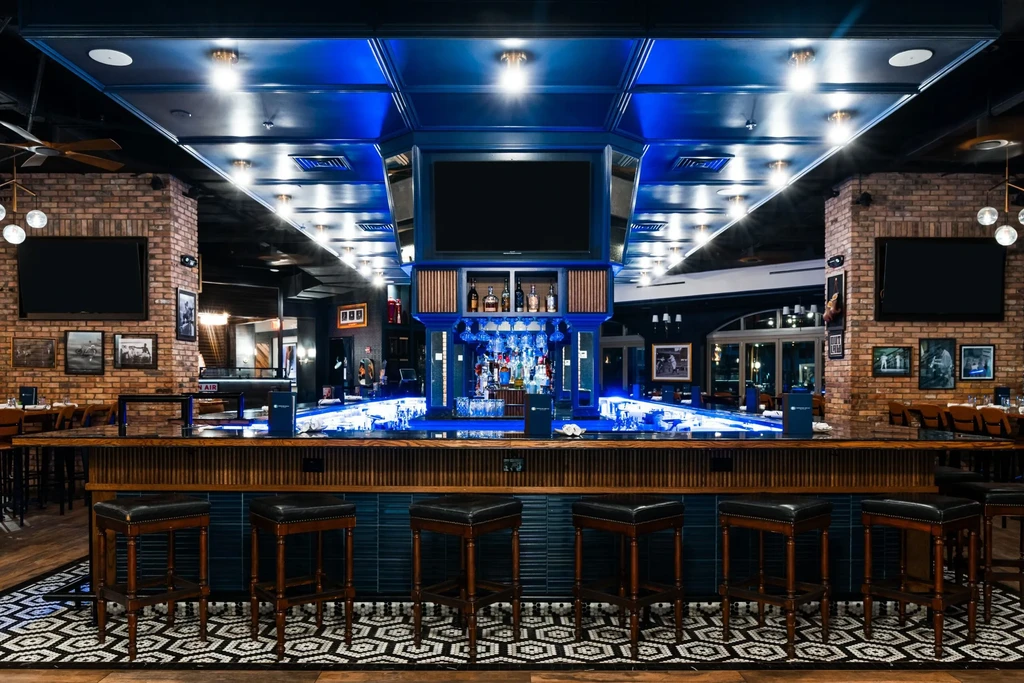 Modern bar interior, prominent blue lighting, leather stools, geometric floor.