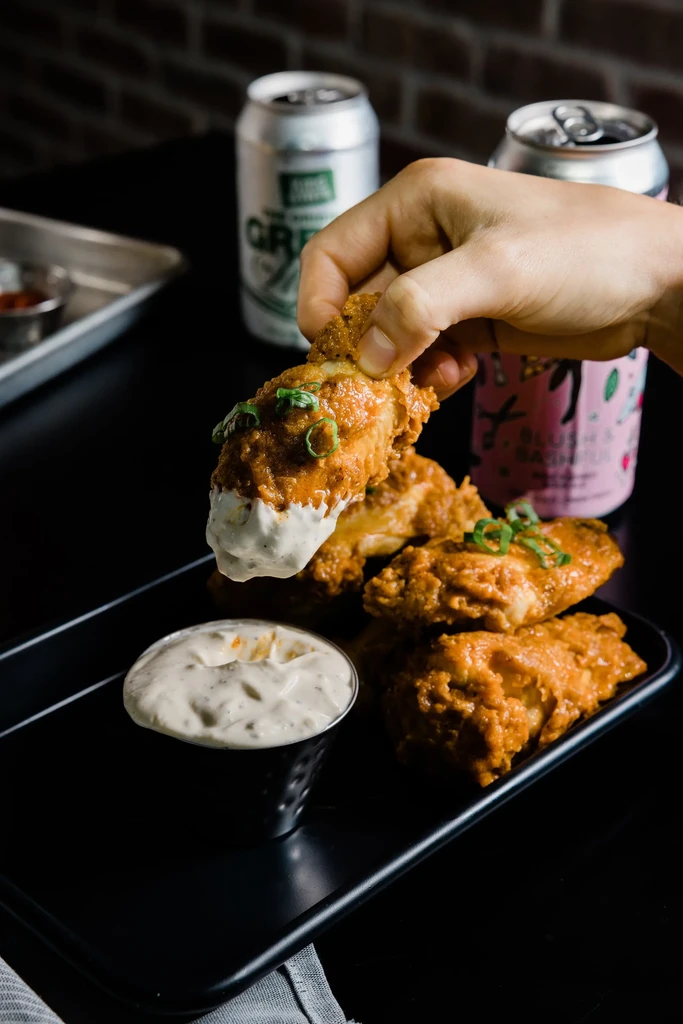Hand dipping crispy fried chicken wing into white creamy sauce.