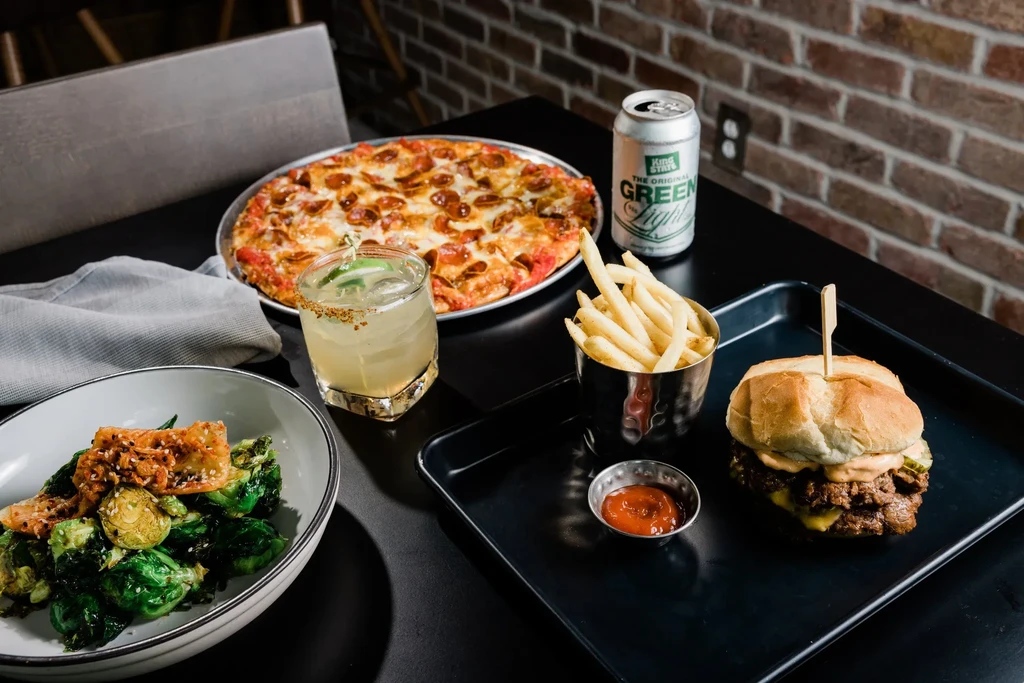 Pepperoni pizza, cheeseburger, fries, sprouts, cocktail, and beer on a table.