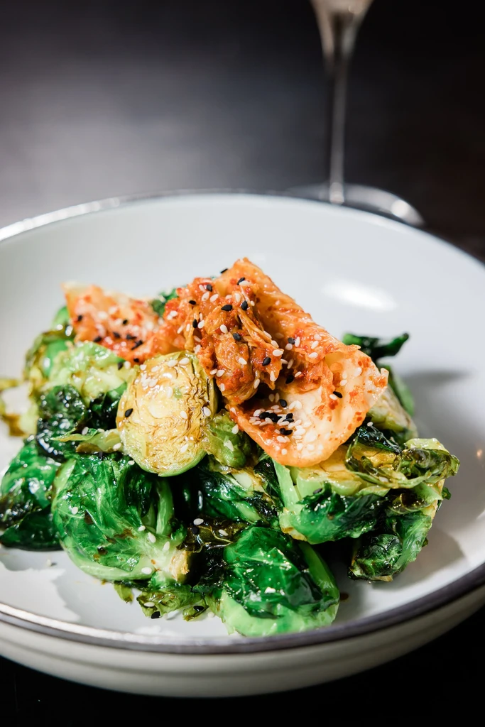 Roasted Brussels sprouts topped with kimchi and white and black sesame seeds.