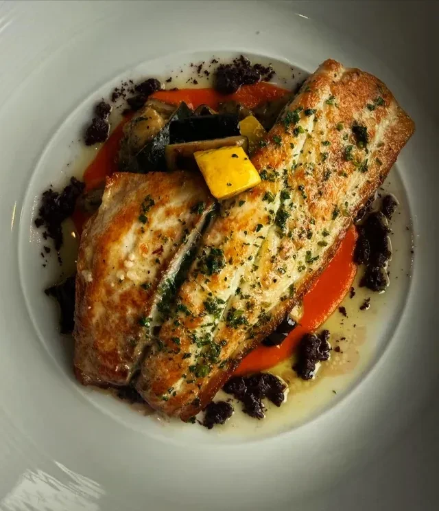Two seared fish fillets, mixed vegetables, orange sauce, and herbs.