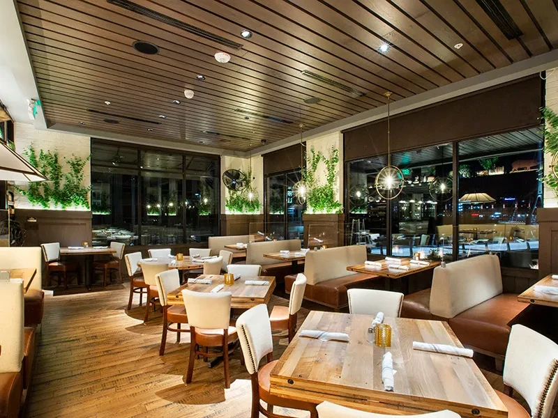 Empty modern restaurant dining room with booths, tables, and warm lighting.