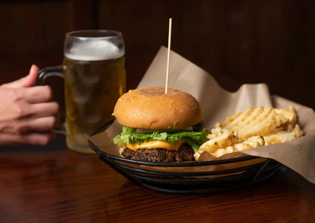Cheeseburger and waffle fries in basket with a frothy beer.