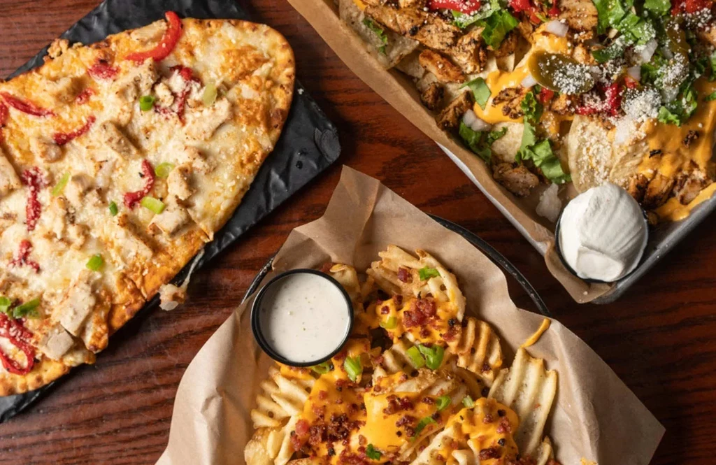 Assortment of chicken flatbread, loaded nachos, and loaded waffle fries.