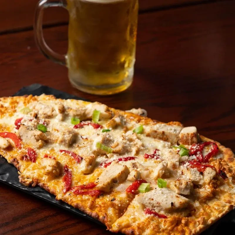 Rectangular flatbread pizza with chicken, cheese, tomatoes, green onions.