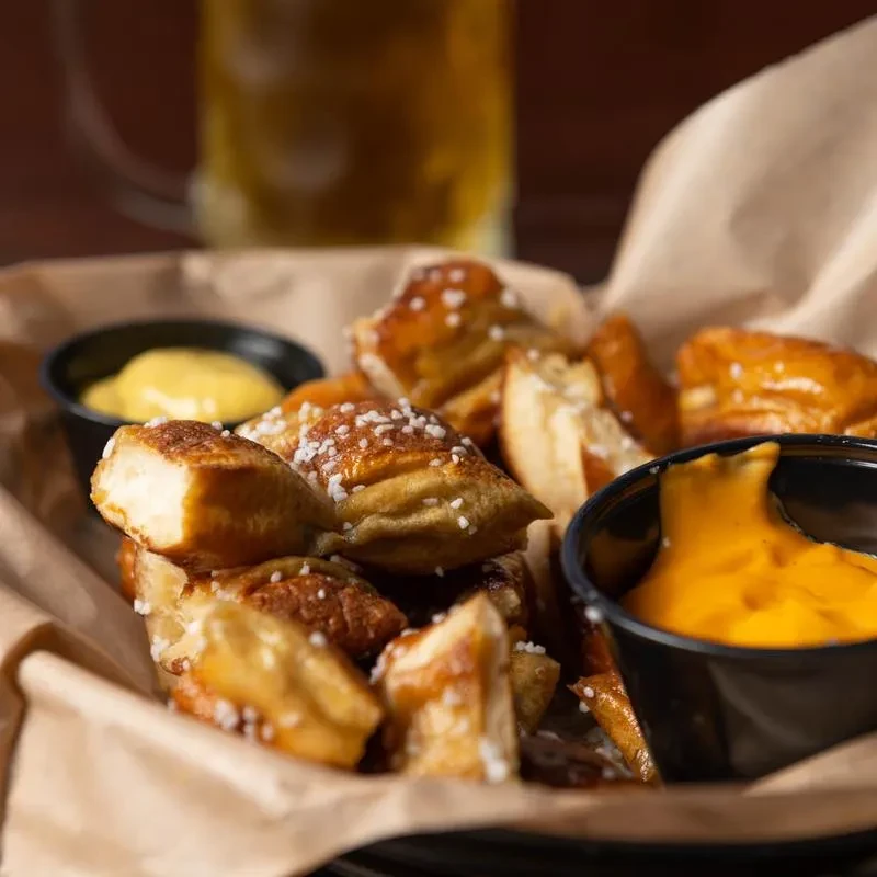 Basket of salted pretzel bites with mustard and cheese sauces.