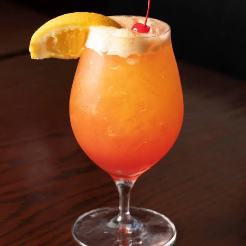 Gradient orange cocktail in a stemmed glass with orange and cherry.