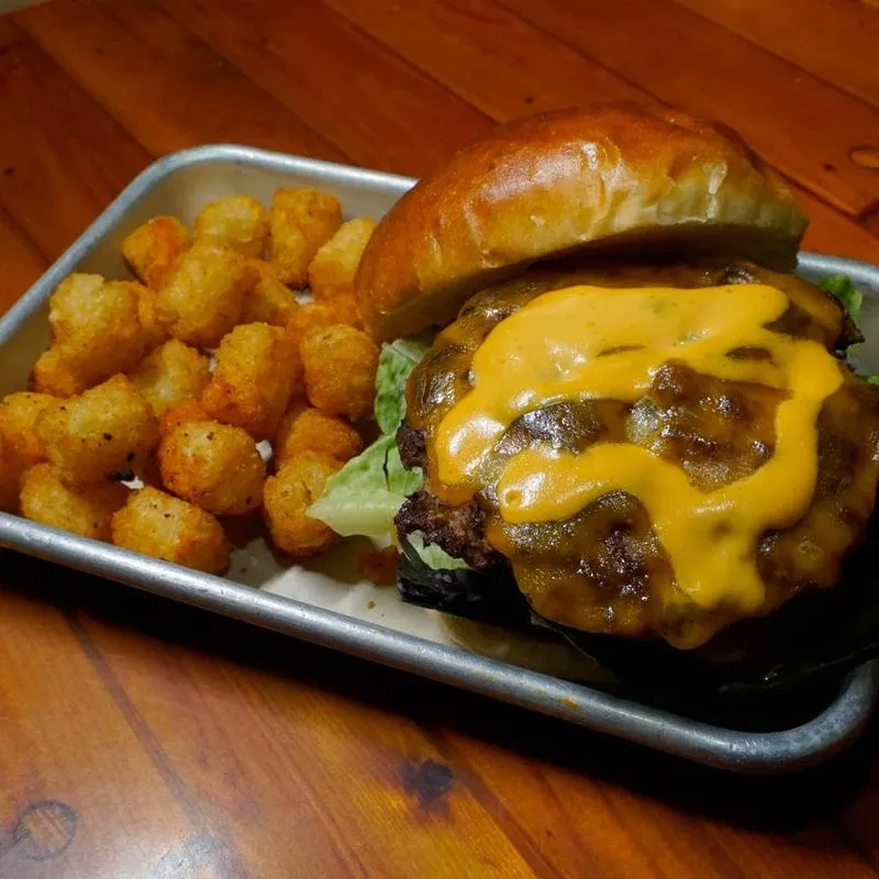 Close-up of a double cheeseburger with melted cheese and crispy tater tots.