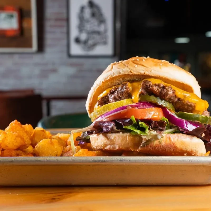 Close-up of a double cheeseburger and crispy tater tots on a silver tray.
