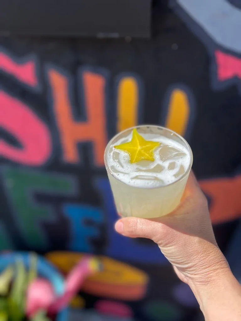 Hand holding a frothy yellow drink with ice and star fruit.