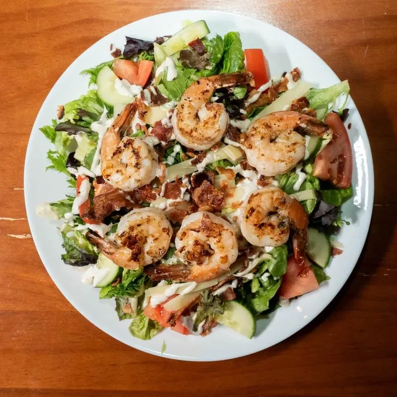 Grilled shrimp salad with mixed greens, tomatoes, bacon, and cheese.