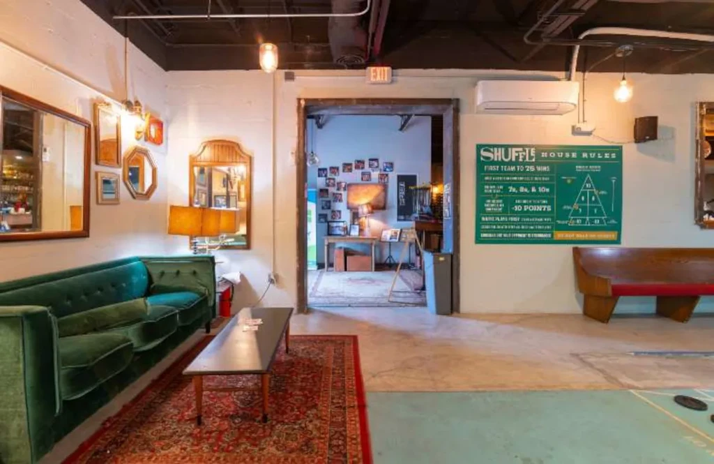 Industrial lounge with green velvet couch and a shuffleboard court.
