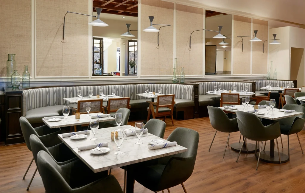 Empty restaurant dining area with marble tables, upholstered chairs, striped booths.