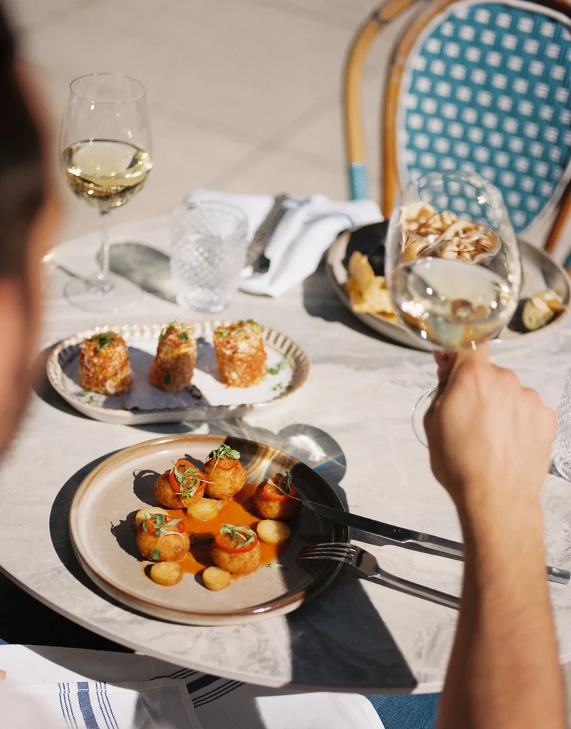 Sunlit table with fried appetizers, two glasses of wine, and water.