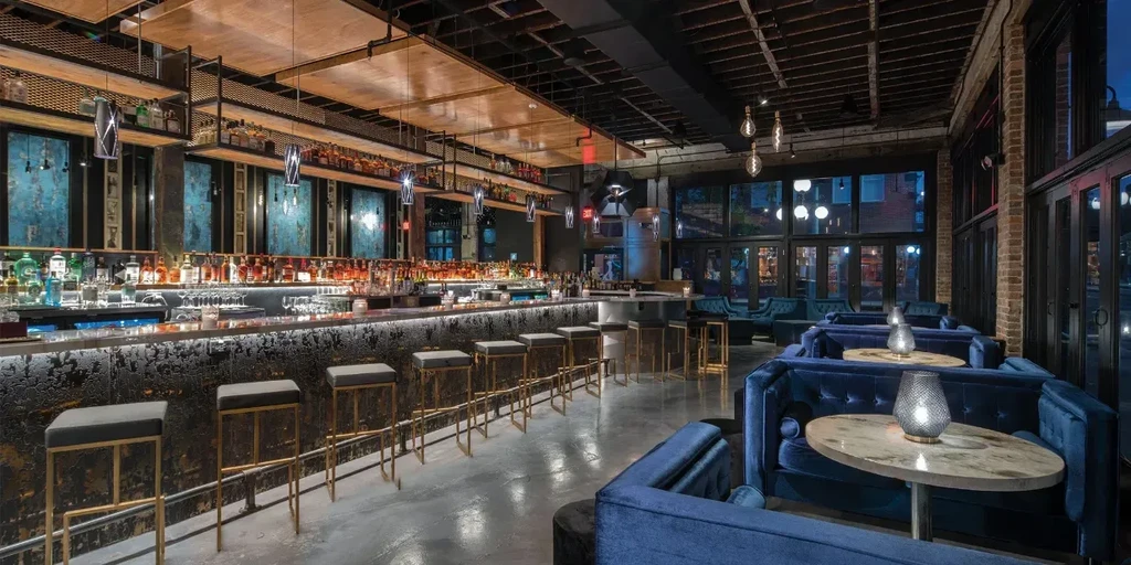 Modern bar and lounge with industrial ceiling, velvet sofas, and city views.