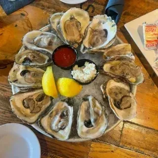 Large platter of raw oysters on ice with lemon and sauces.