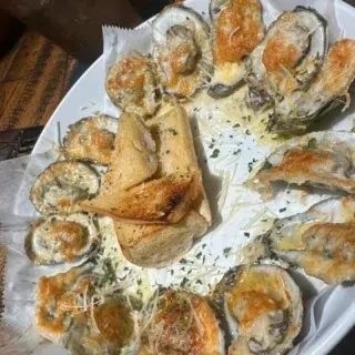 A white plate filled with bubbling baked oysters and garlic bread.