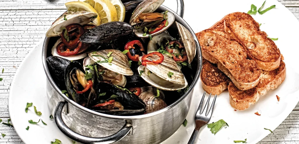 Rustic pot of cooked mussels, clams, herbs, lemon, with toasted bread.