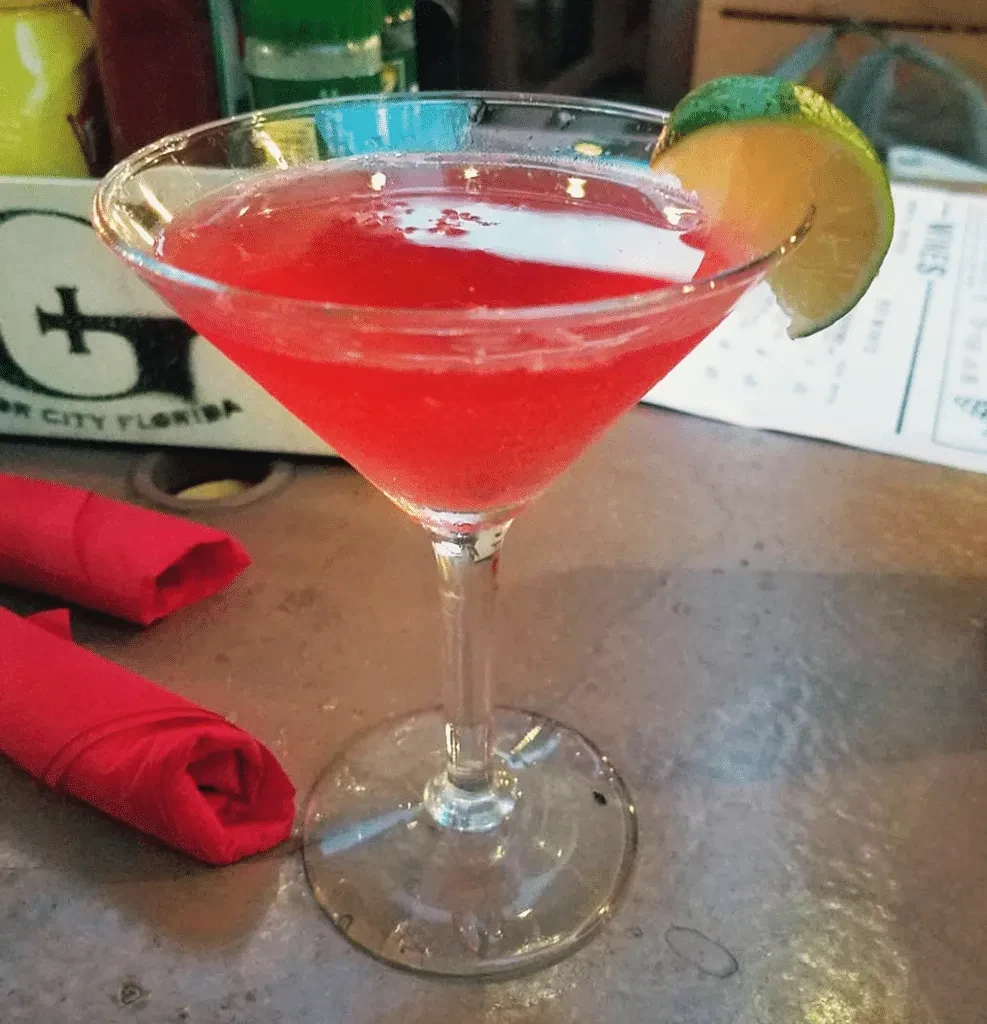 Vibrant red cocktail in martini glass with lime garnish.