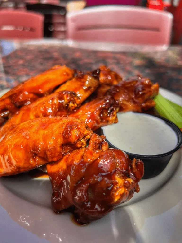 A plate of red hot wings with dip and celery at a restaurant.
