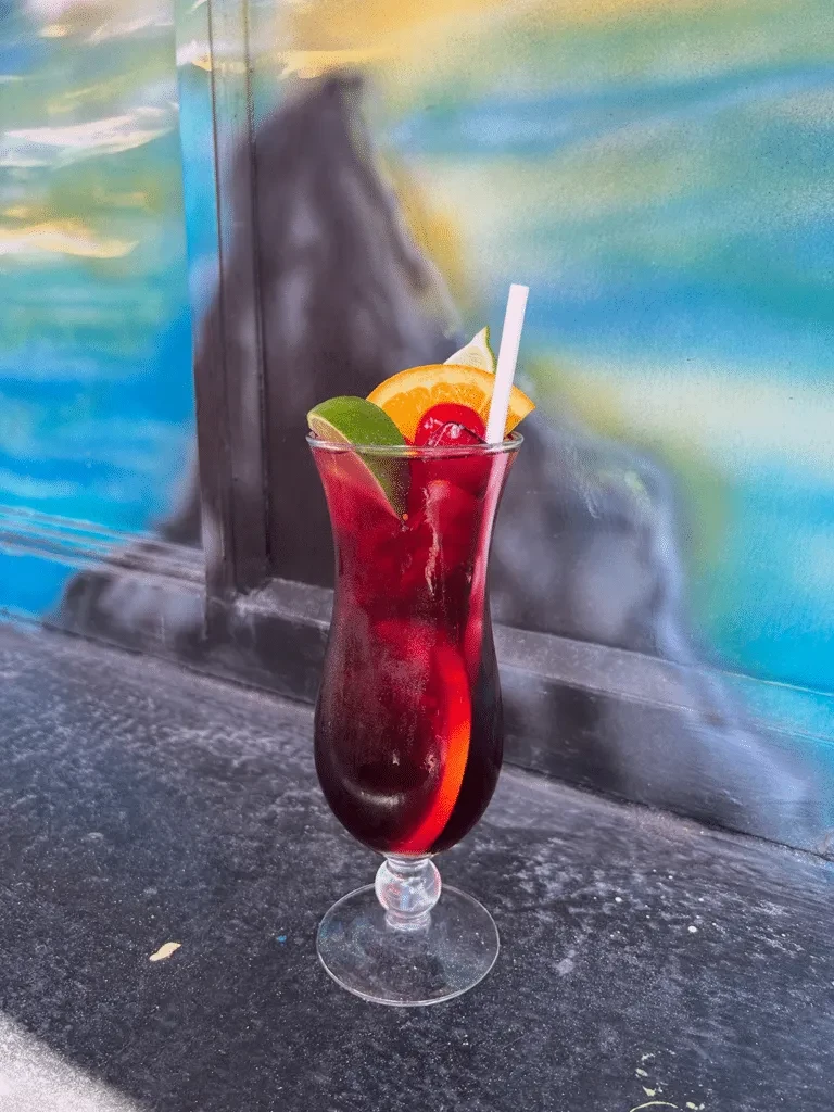 Deep red cocktail in hurricane glass with citrus and cherries.