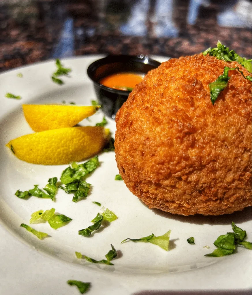 Golden-brown deep-fried food on plate with lemon and sauce.