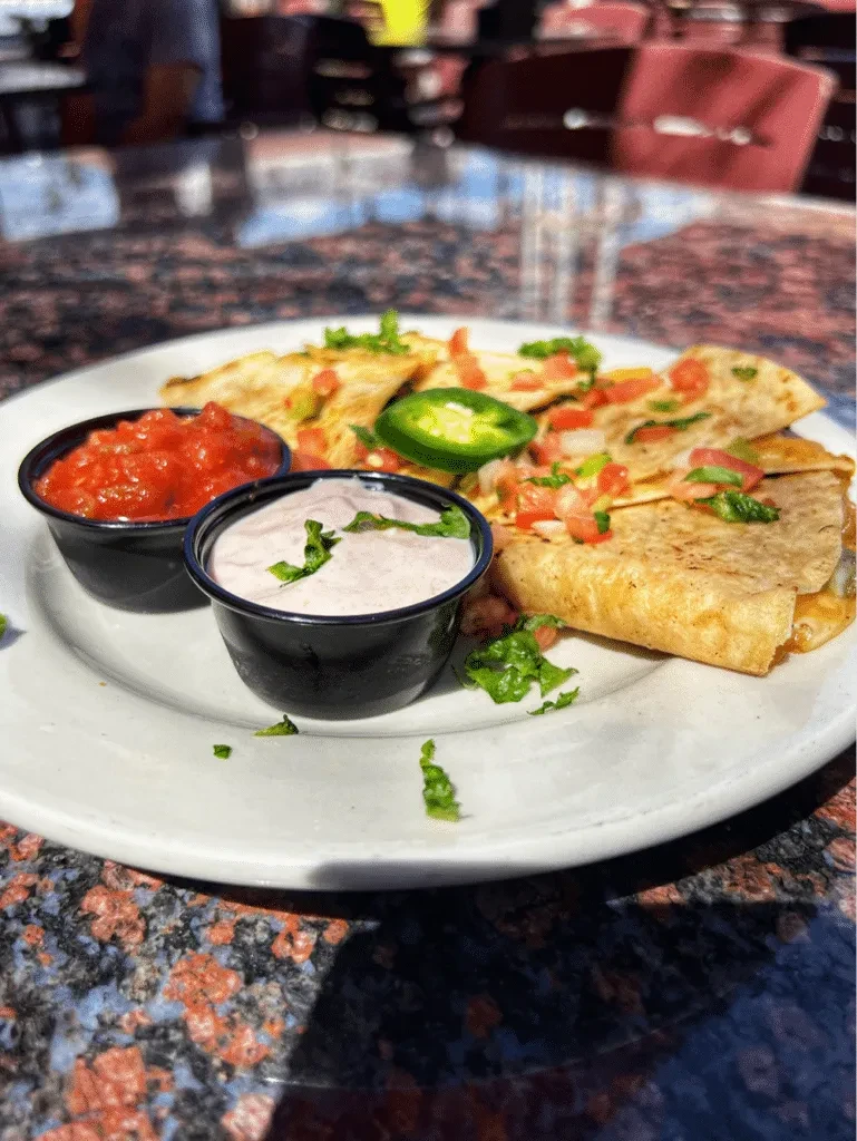 Quesadilla pieces topped with tomatoes, cilantro, jalapeño, red salsa, and pink crema.