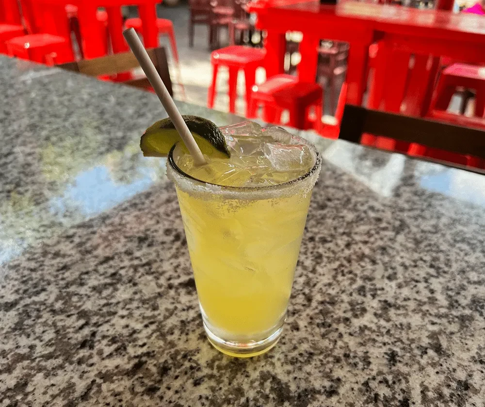 Icy yellow cocktail with salted rim, lime, and straw.