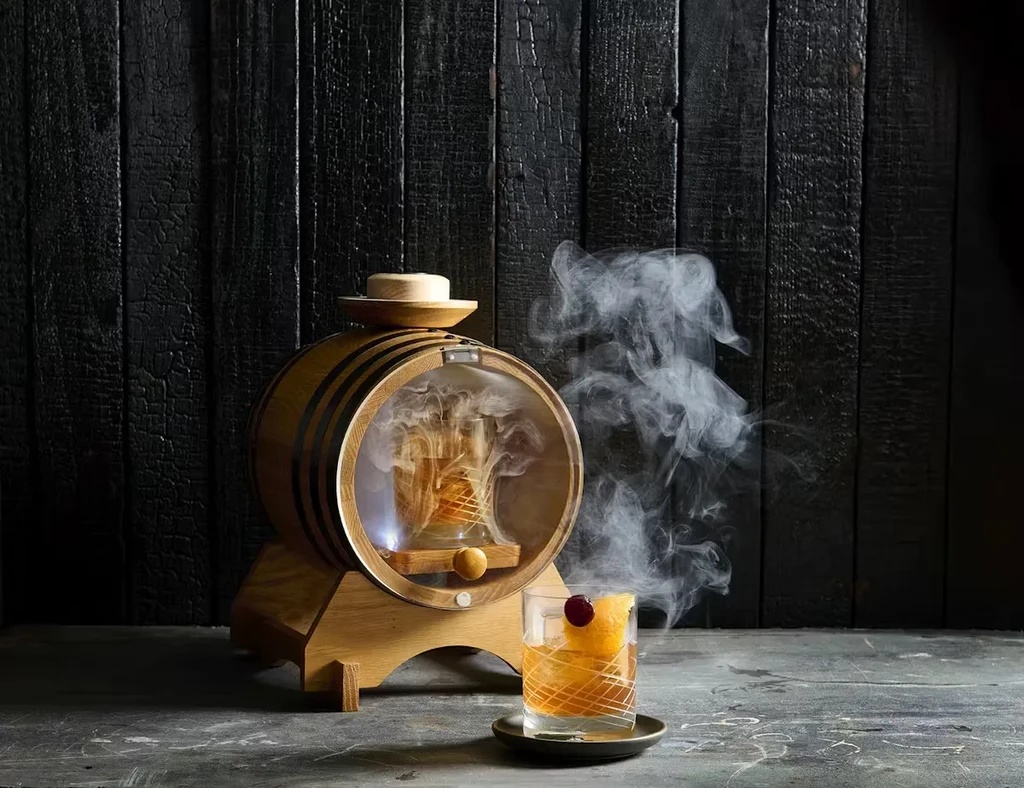 Cocktails being smoked; one in a barrel, one in a rocks glass.