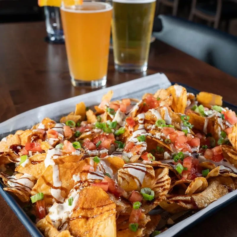 Close-up of loaded potato chips with tomatoes, green onions, and two sauces.